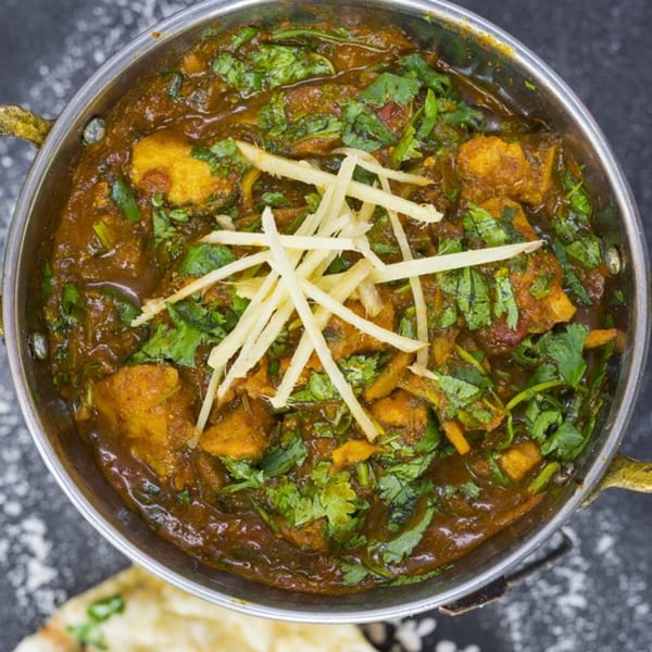 Taj Mahal Homestyle Indian and Pakistani Cuisine's chicken curry, garnished with cilantro and ginger, in a metal bowl.