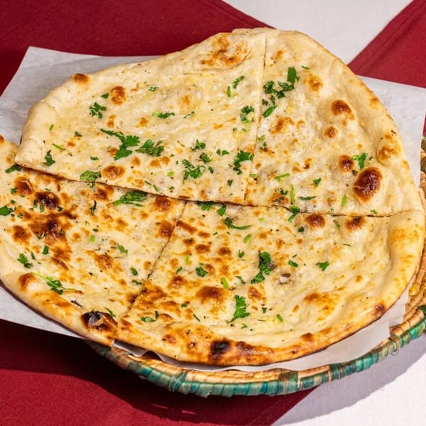 Golden-brown naan bread, garnished with fresh cilantro, served in a woven basket on a red and white tablecloth.