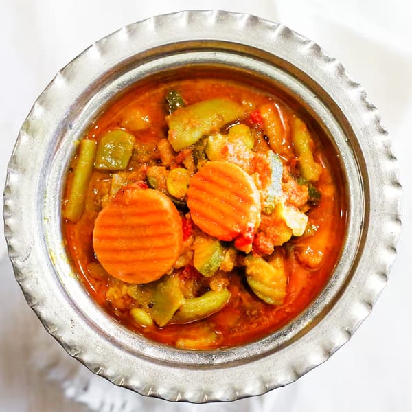A close-up of a silver bowl filled with a vibrant Indian vegetable curry, featuring carrots and green beans.