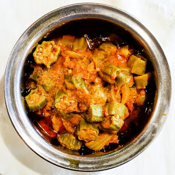 A close-up, top-down view of a metal bowl filled with a rich, orange-red okra curry.