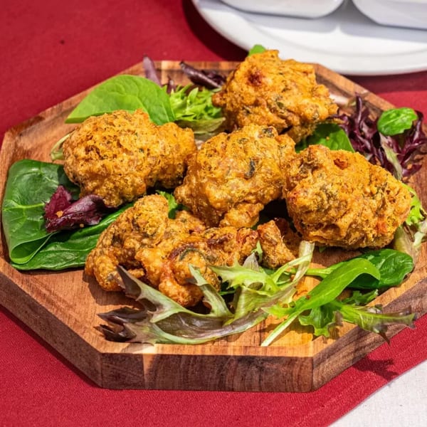 Golden-brown Indian pakoras, garnished with fresh green and red lettuce, on a wooden serving board.