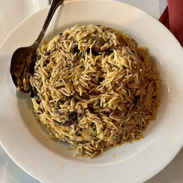 A large serving of Indian biryani with rice and meat, served on a white plate with a spoon.