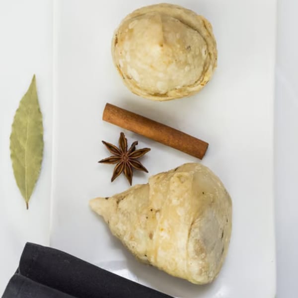 Two Indian samosas on a white plate with a bay leaf, cinnamon stick, and star anise.